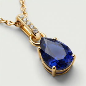 A close view shows the blue sapphire facets, gold prongs, and five clear stones along the bail.