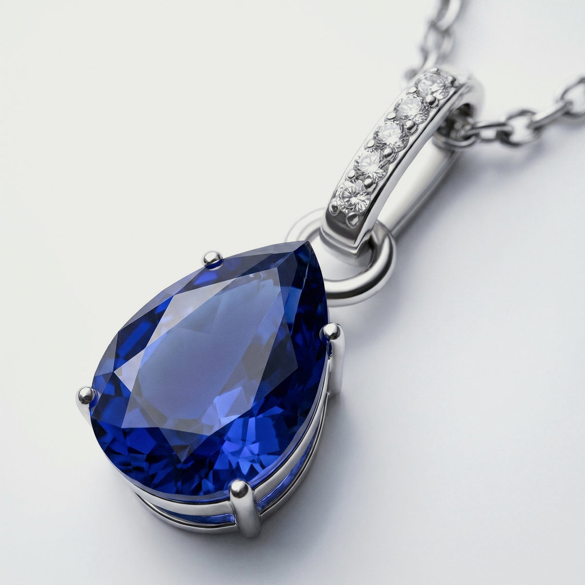 The silver pendant is shown close up with its blue faceted stone, rounded prongs, and polished connecting ring.