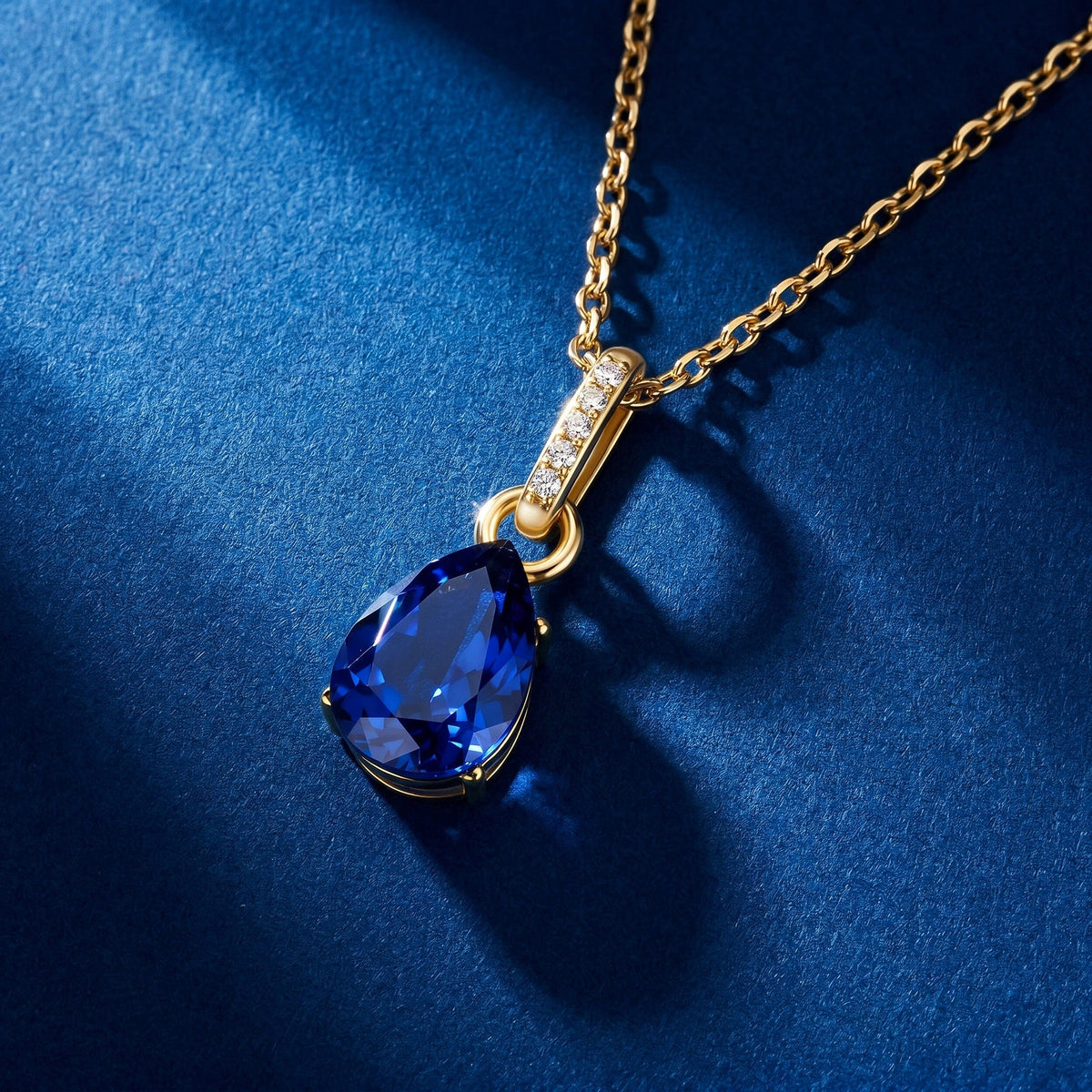 The gold sapphire pendant and cable chain lie diagonally across a clean blue textured surface.