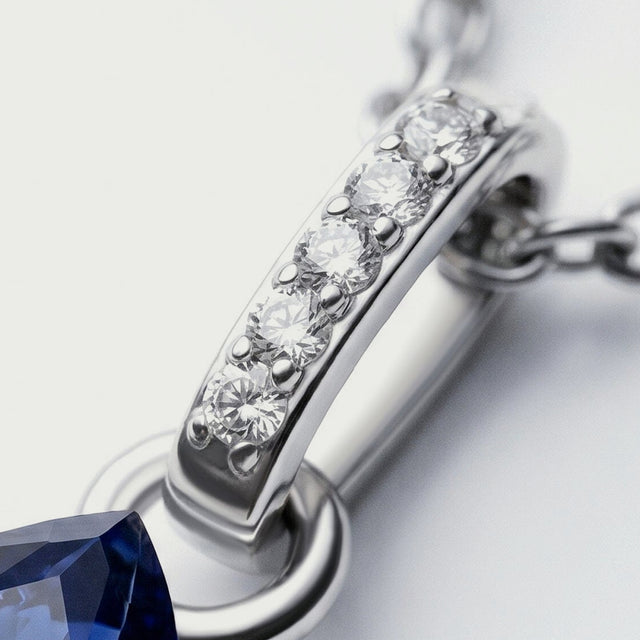 Five clear round stones line the silver bail beside oval chain links and the top of the blue sapphire.