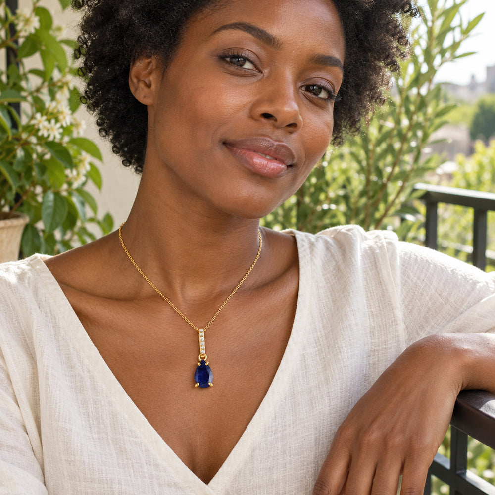 A woman in an ivory linen blouse wears the gold blue sapphire necklace on a leafy veranda.