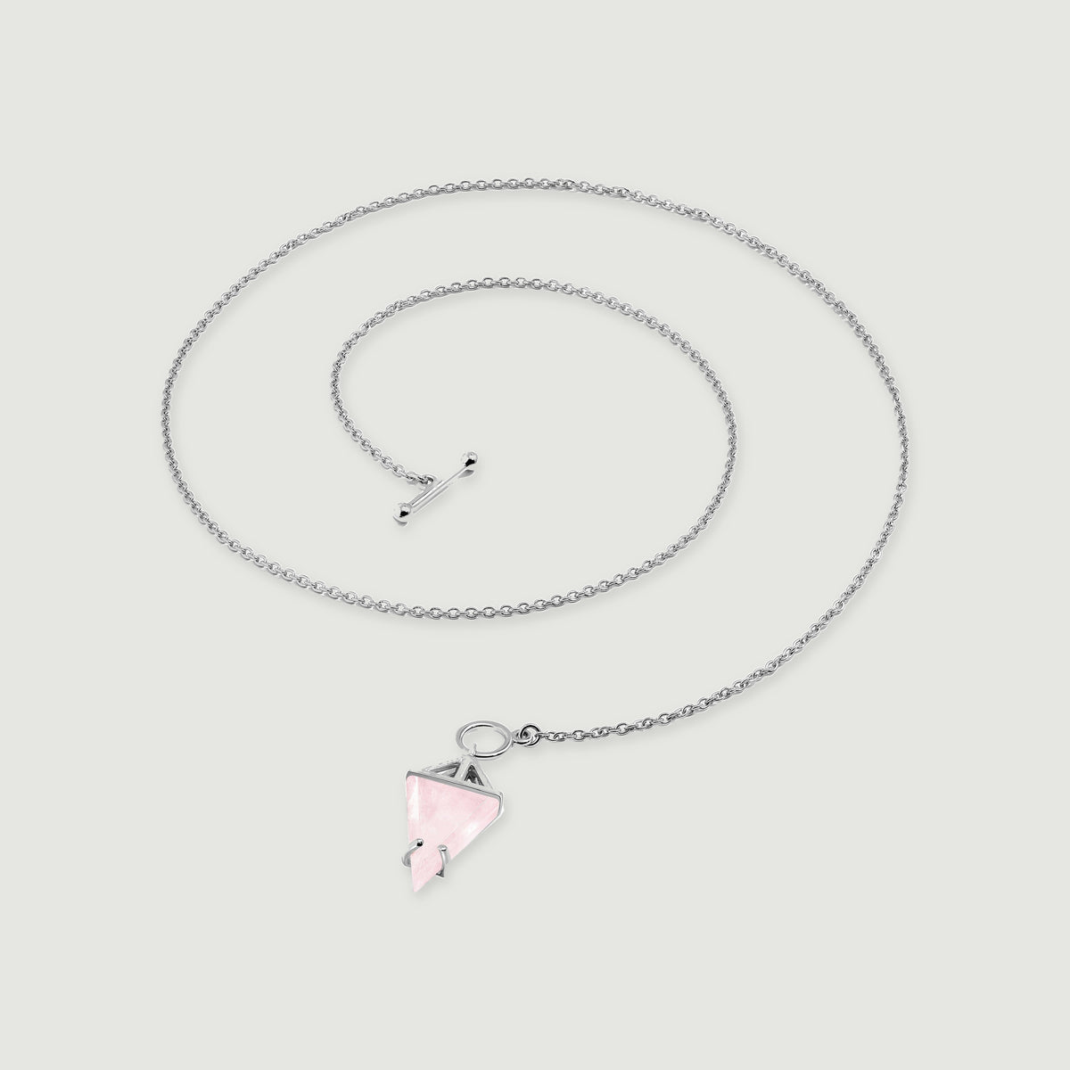 The silver necklace forms a loose coil with its pointed pink pendant resting below the open circular clasp.