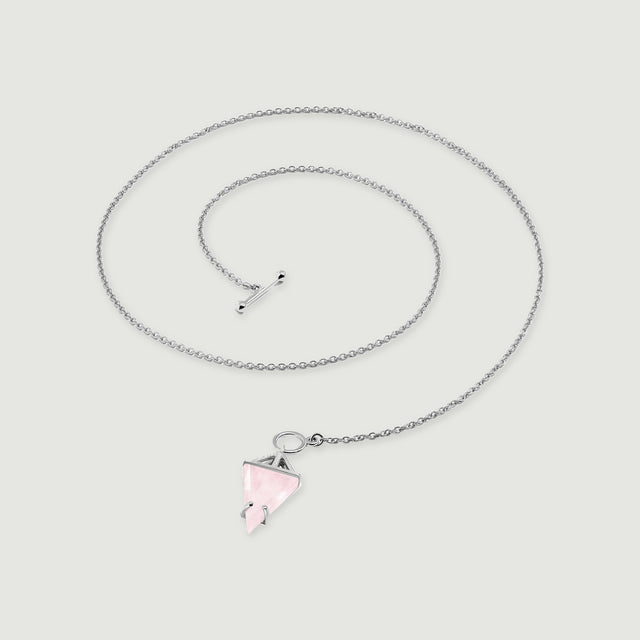 The silver necklace forms a loose coil with its pointed pink pendant resting below the open circular clasp.