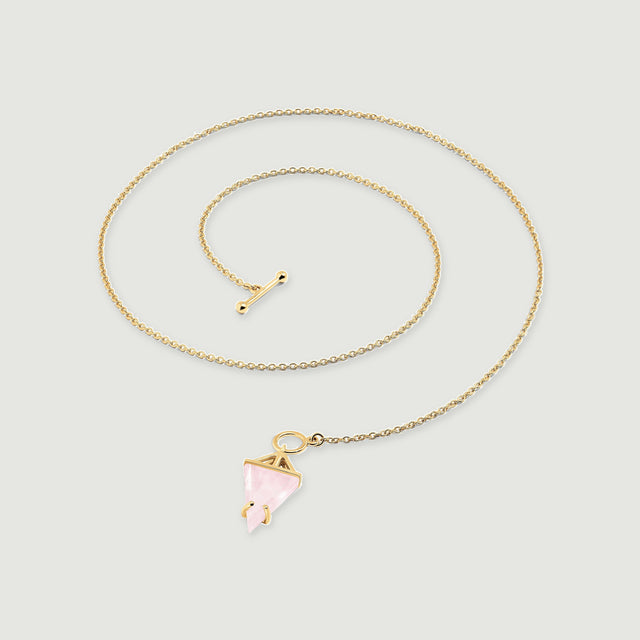 A yellow gold necklace is laid in a curved coil with a pink triangular stone and a separate toggle bar.