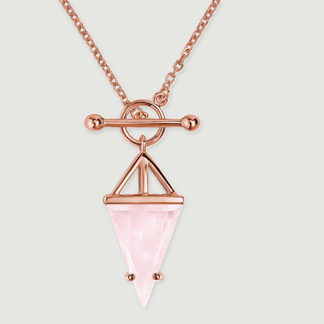 Warm rose gold prongs hold the tapered pink stone below an open geometric frame and circular fastening.
