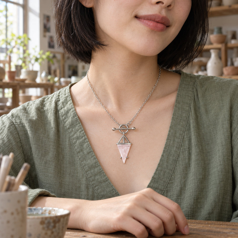 A woman in a sage linen blouse wears the silver rose quartz necklace at a wooden pottery table.