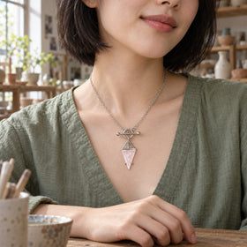 A woman in a sage linen blouse wears the silver rose quartz necklace at a wooden pottery table.
