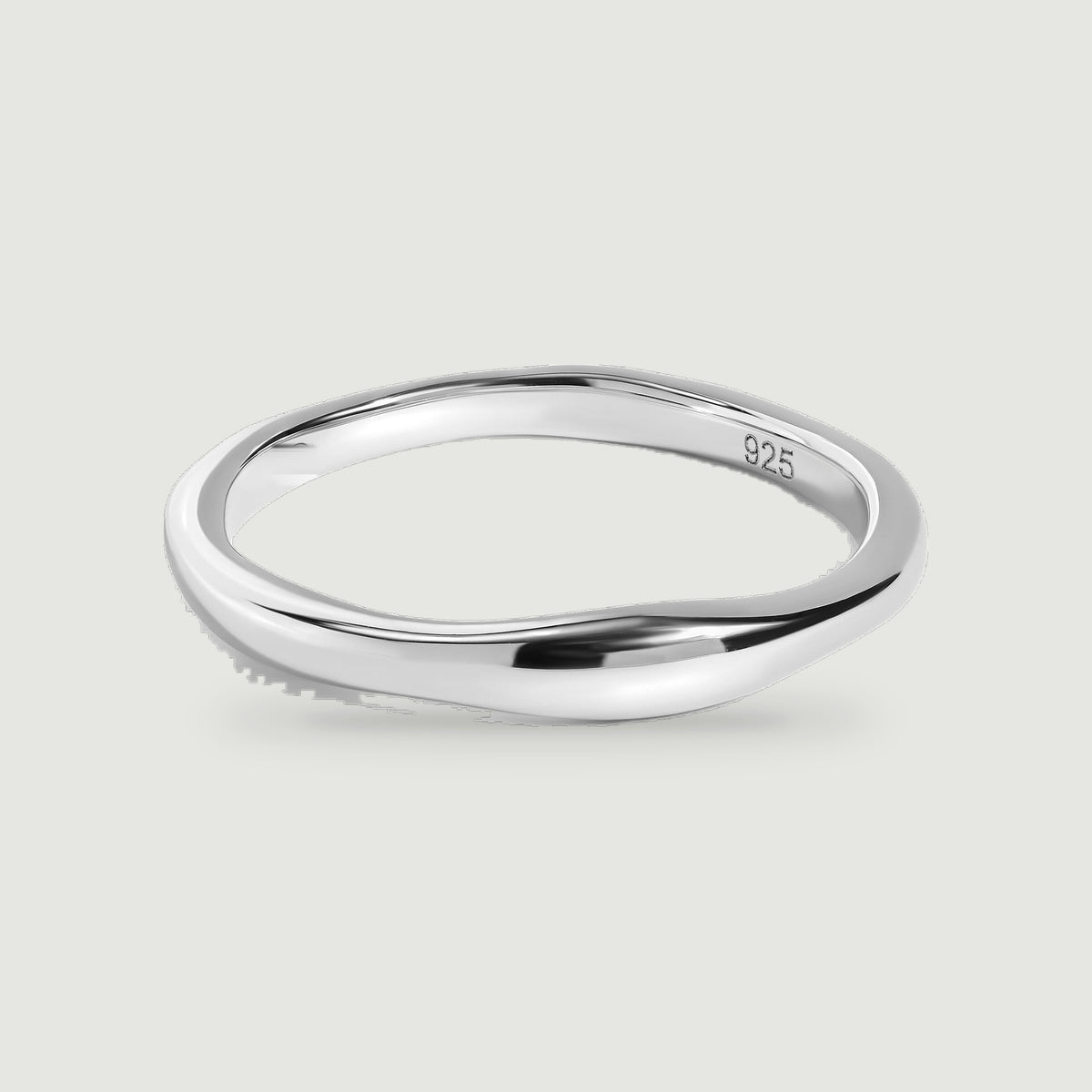 A polished silver ring with a gently contoured band rests on a pale gray surface.