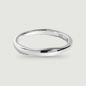 A polished silver ring with a gently contoured band rests on a pale gray surface.