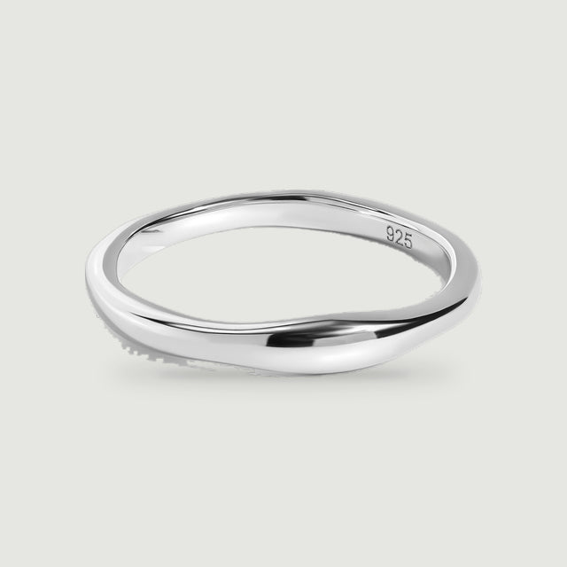 A polished silver ring with a gently contoured band rests on a pale gray surface.