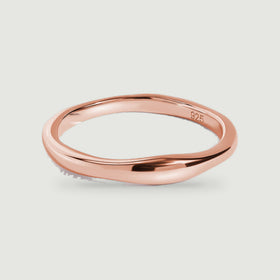 A rose gold ring displays its rounded profile and reflective finish on a gray background.
