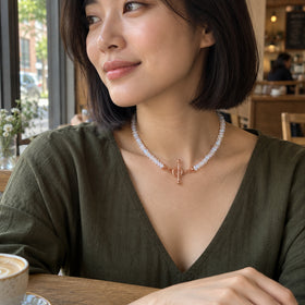 A woman with a dark bob wears the moonstone necklace over an olive neckline beside a cafe window.