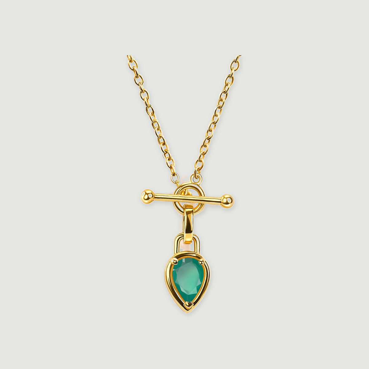 A yellow gold plated necklace has a pear-shaped green stone suspended below a polished bar and circular clasp.