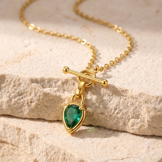 A gold-toned necklace rests across pale textured stone with its green pendant hanging over the edge.