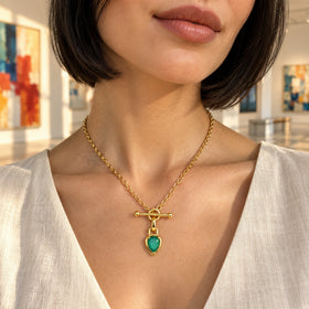 A woman in an ivory linen top wears the gold-toned green pendant necklace in a sunlit gallery.