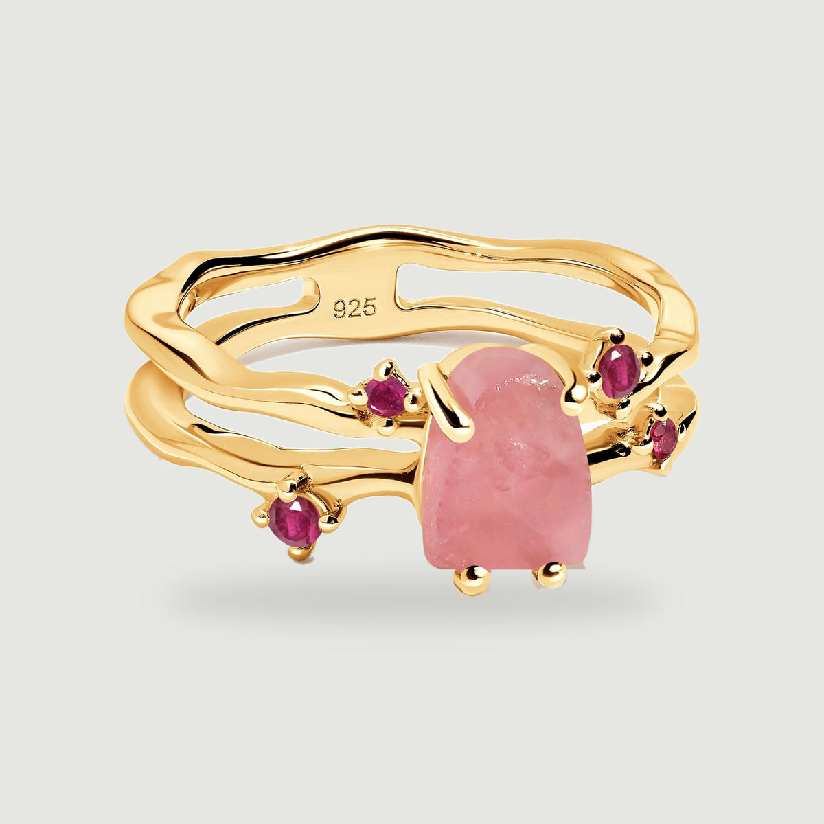 A yellow gold vermeil ring displays a rough pink rose quartz center and four ruby accents on a light gray surface.