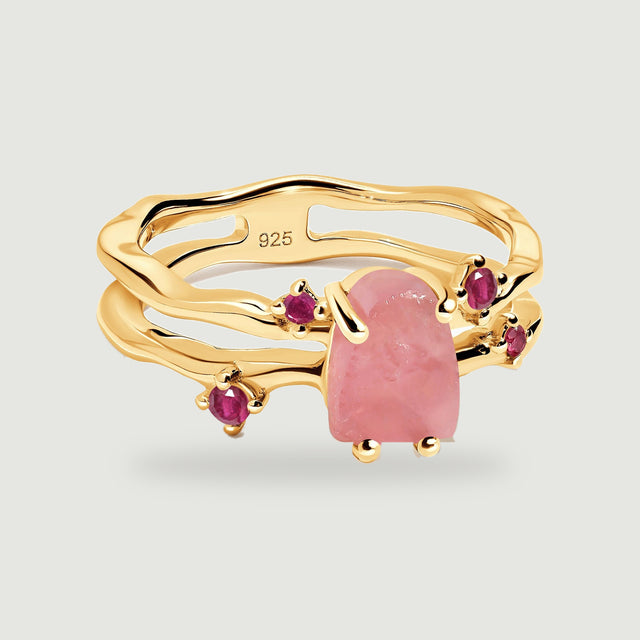 A yellow gold vermeil ring displays a rough pink rose quartz center and four ruby accents on a light gray surface.