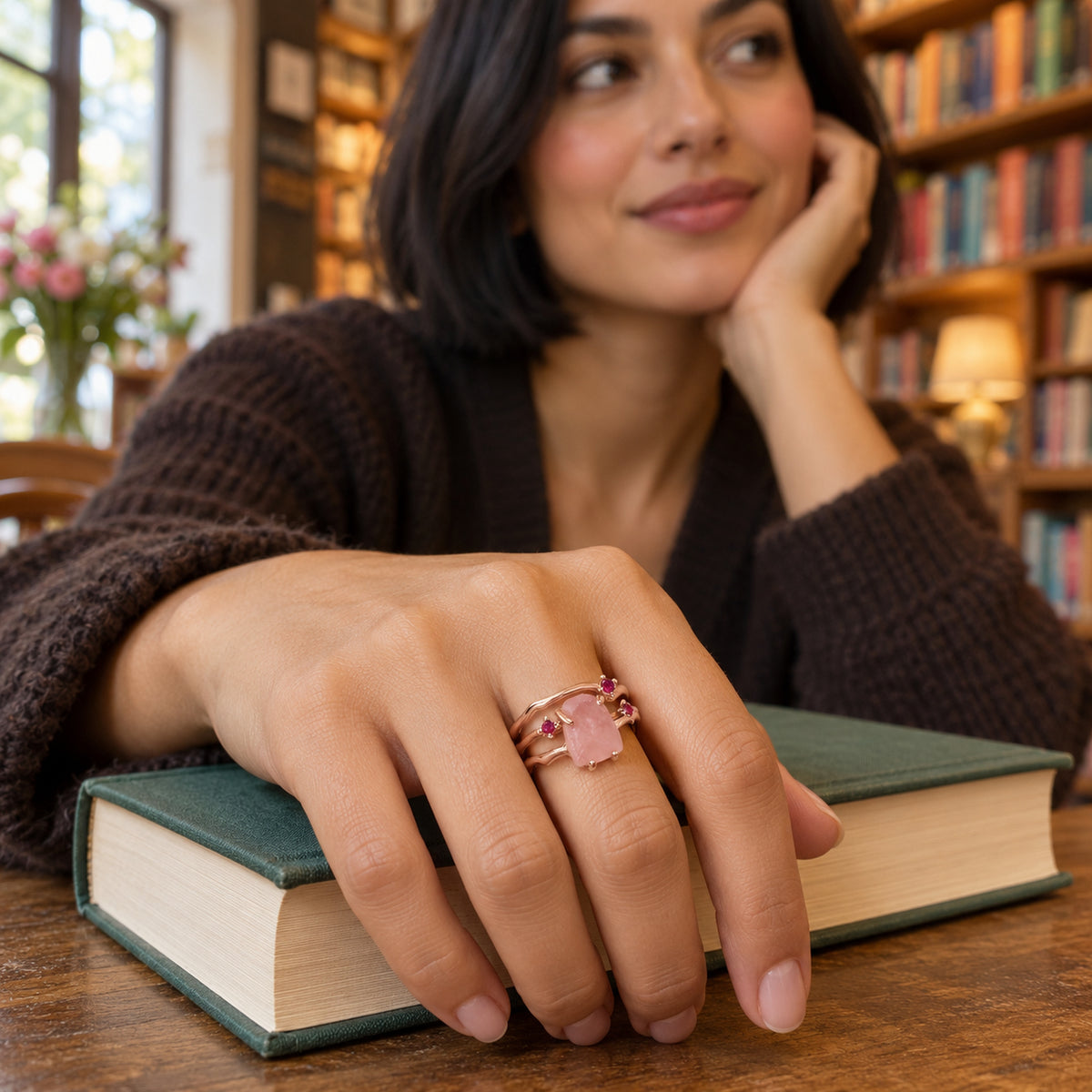 A rose gold vermeil ring with pink rose quartz and ruby accents is worn on a hand resting on a green book.