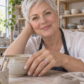 A woman wears a sterling silver rose quartz and ruby ring beside a ceramic bowl in a pottery studio.