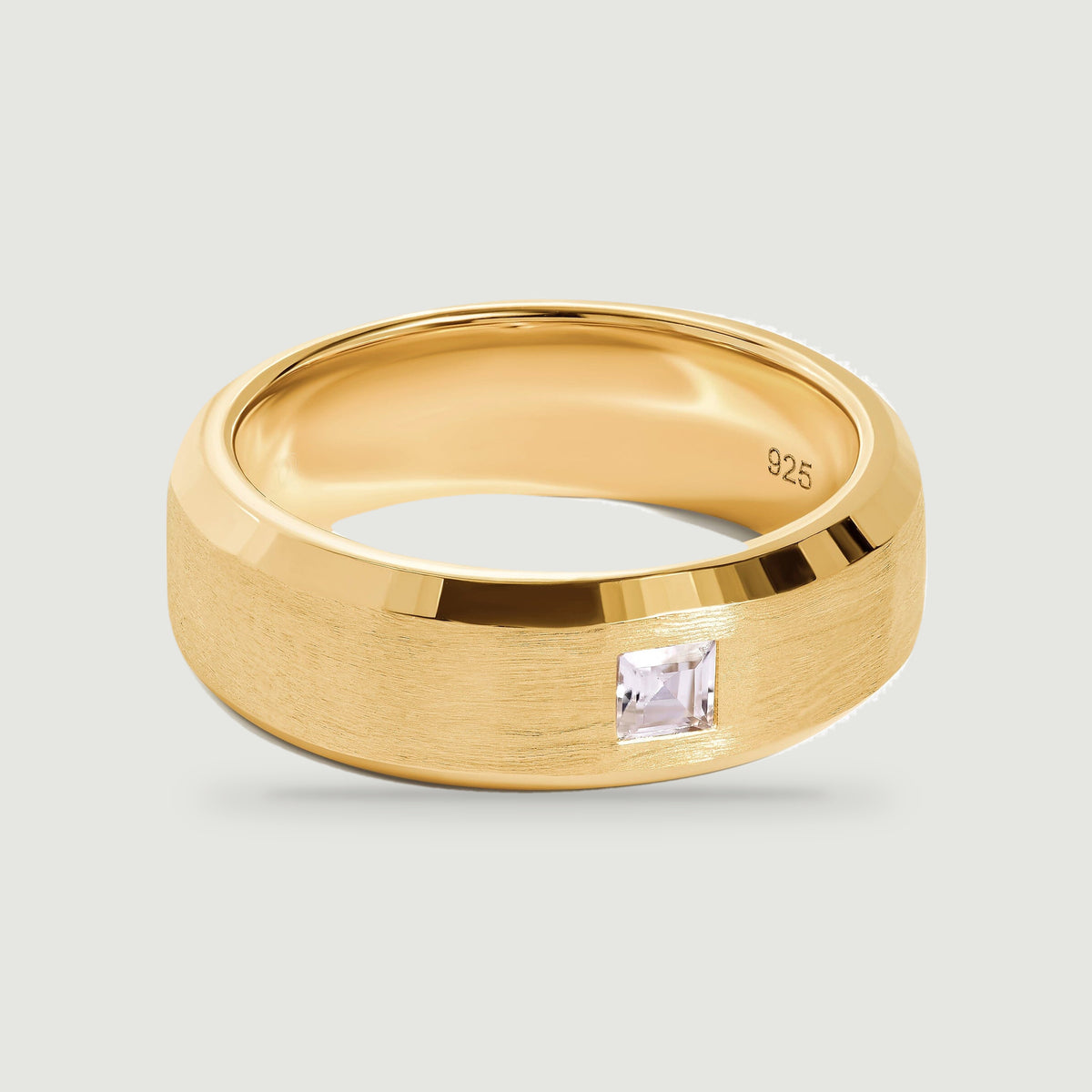 A yellow gold ring shows a square clear stone between polished edges and a brushed center.