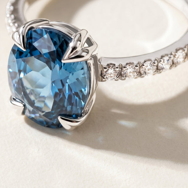 A close view shows blue gemstone facets, polished silver claws and round clear stones on a pale stone tabletop.