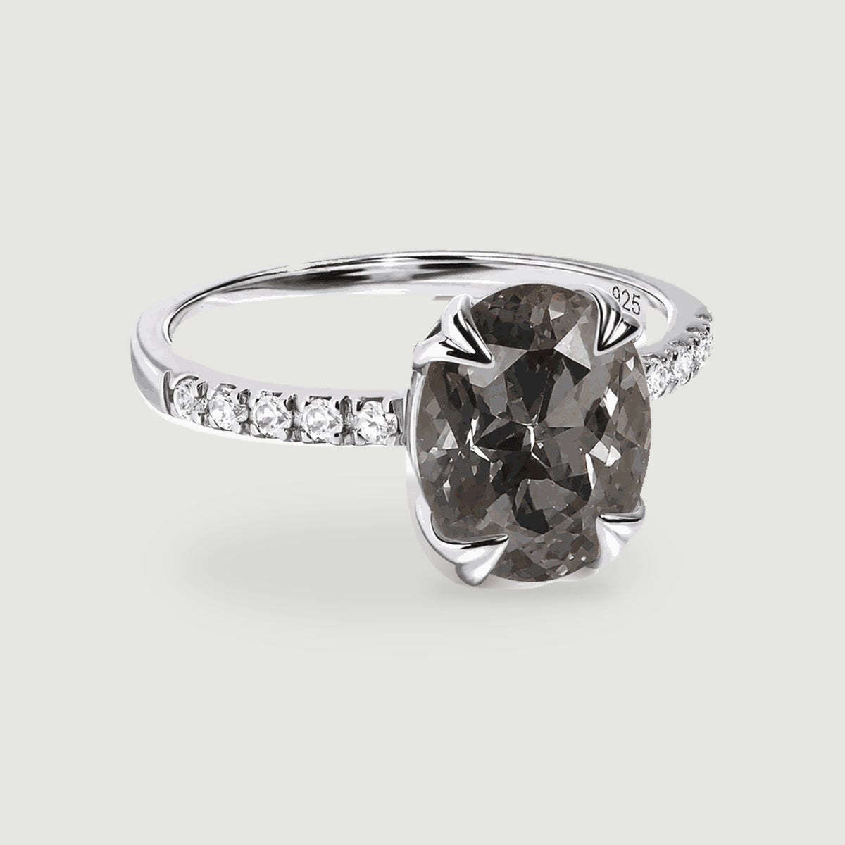 A three-quarter view shows a grey oval gemstone held by silver claws above a slim band with clear shoulder stones.