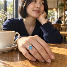 A woman with a short black bob wears a silver blue gemstone ring while resting her hand beside a ceramic cup in a cafe.