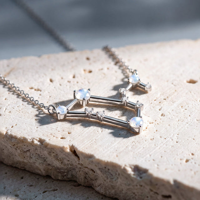 A silver necklace rests across a stone slab with its chain extending toward the upper corners.