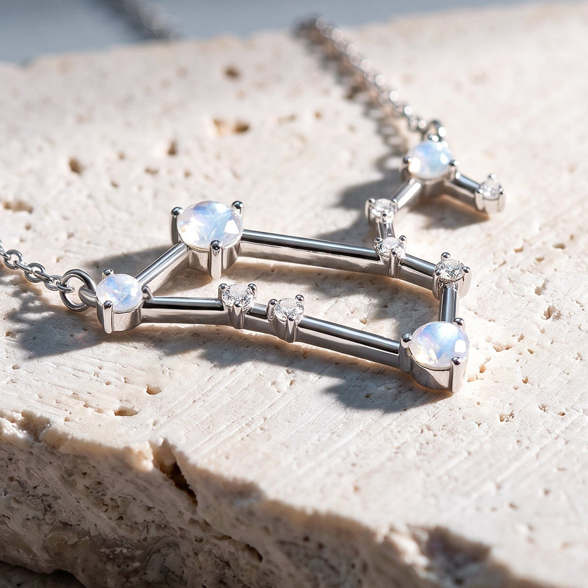 An angled close view reveals raised silver settings and geometric connecting bars above a stone surface.