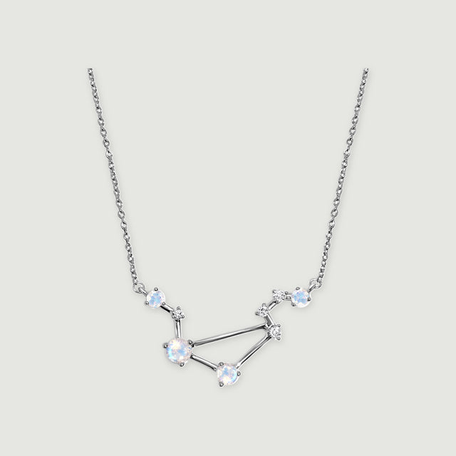 A silver necklace with four round moonstones and small clear stones rests on a light gray background.