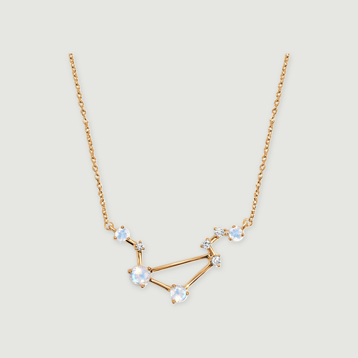 A yellow gold necklace forms an angular constellation with pale blue moonstones on a light gray background.