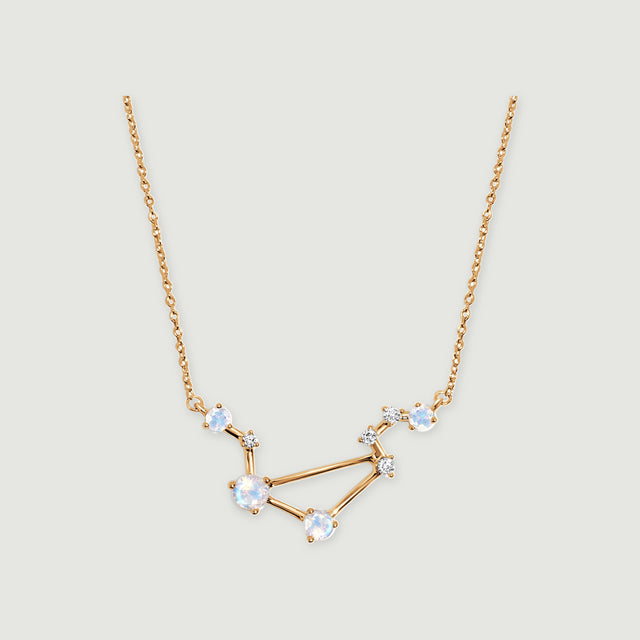 A yellow gold necklace forms an angular constellation with pale blue moonstones on a light gray background.
