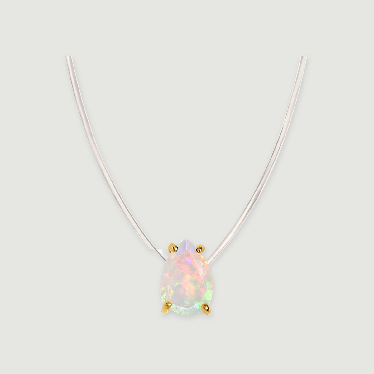 Four yellow gold prongs hold an iridescent pear-shaped opal below a clear curved cord on a pale gray background.