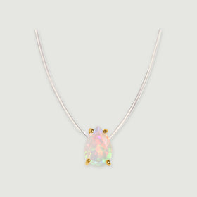 Four yellow gold prongs hold an iridescent pear-shaped opal below a clear curved cord on a pale gray background.