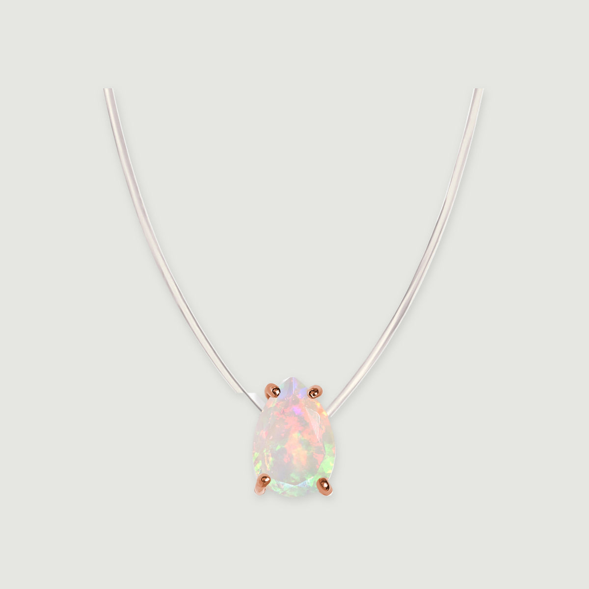 A drop-shaped opal framed by four rose gold prongs sits beneath a transparent cord on a light gray surface.