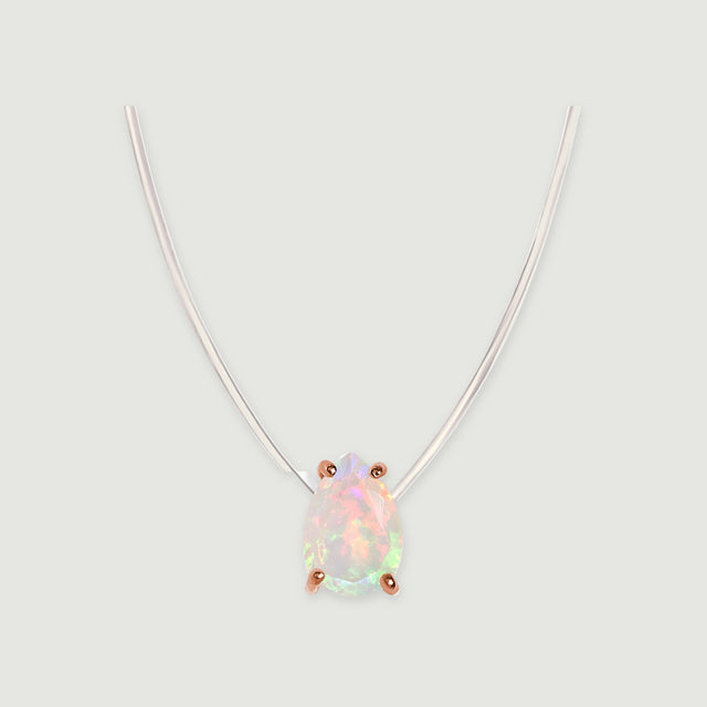 A drop-shaped opal framed by four rose gold prongs sits beneath a transparent cord on a light gray surface.