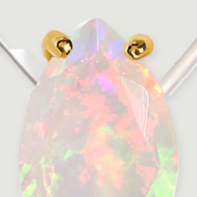 The pointed top of an opal and two polished yellow gold prongs fill this close-up on a pale gray background.