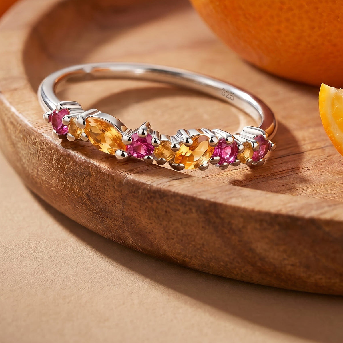 The sterling silver gemstone ring lies on a wooden tray beside orange fruit.