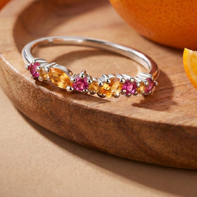 The sterling silver gemstone ring lies on a wooden tray beside orange fruit.