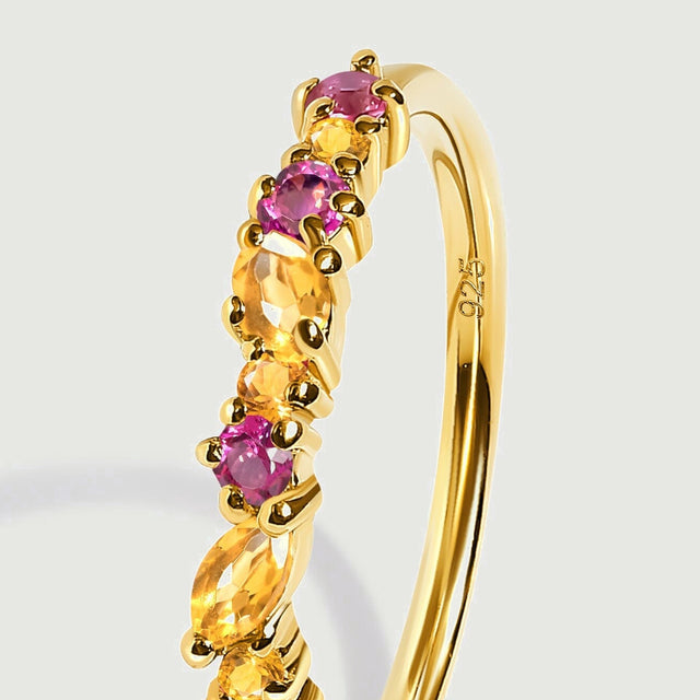 An oblique close view shows the gold band and raised prongs beside orange citrine and round pink topaz.