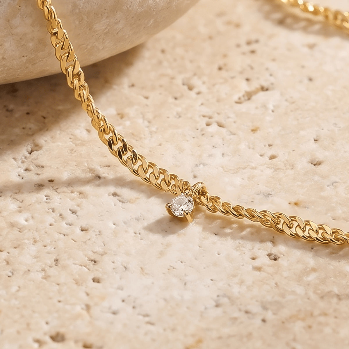A close view shows yellow gold chain links and a clear gemstone drop beside the edge of a pale stone.