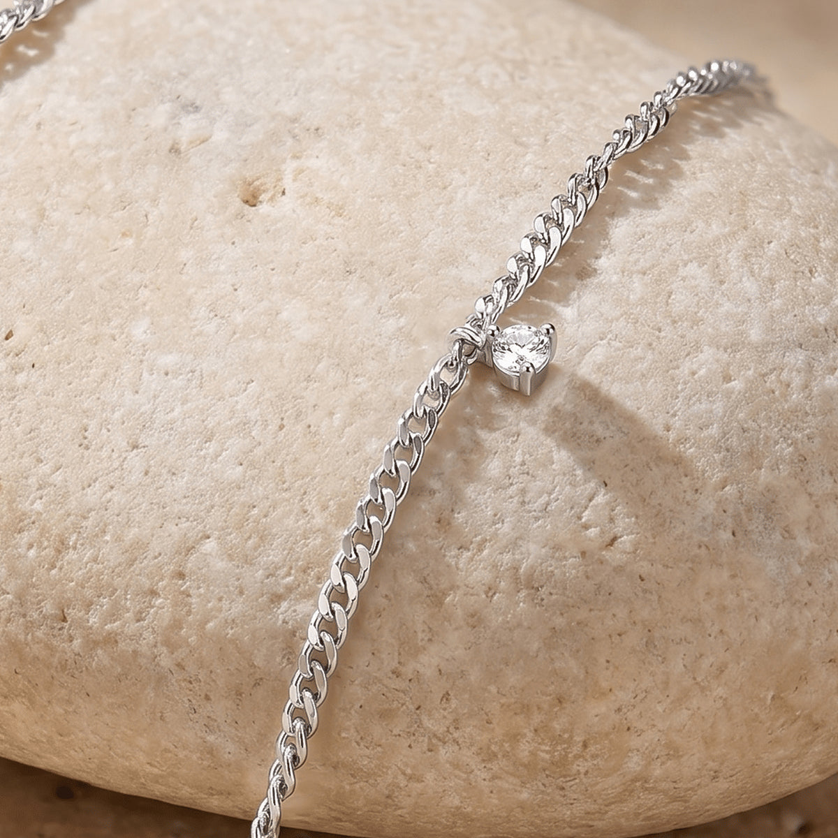 A small clear gemstone setting projects from silver chain links along the curved edge of a pale stone.