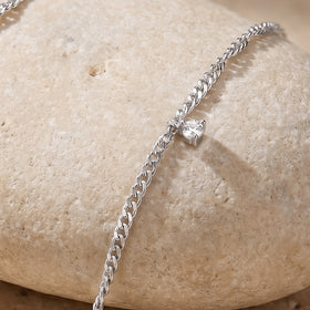 A small clear gemstone setting projects from silver chain links along the curved edge of a pale stone.