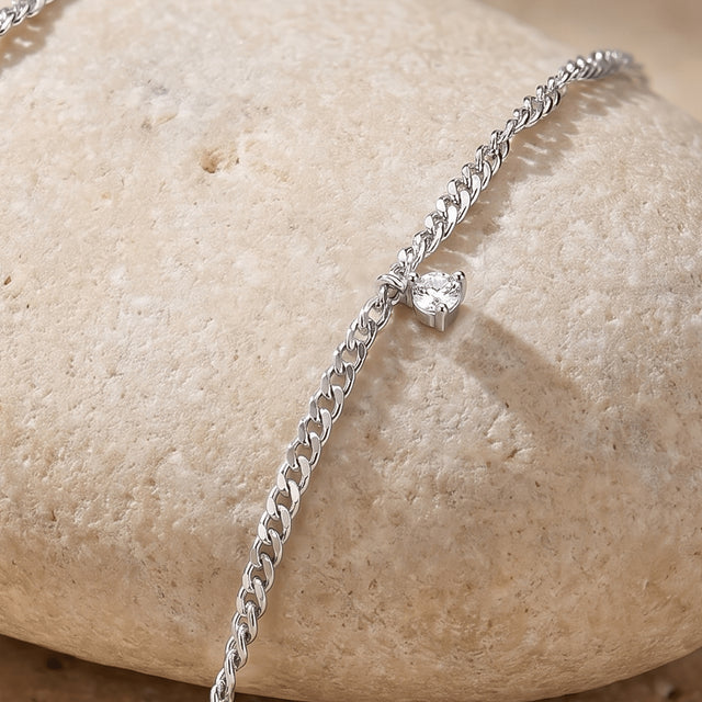 A small clear gemstone setting projects from silver chain links along the curved edge of a pale stone.