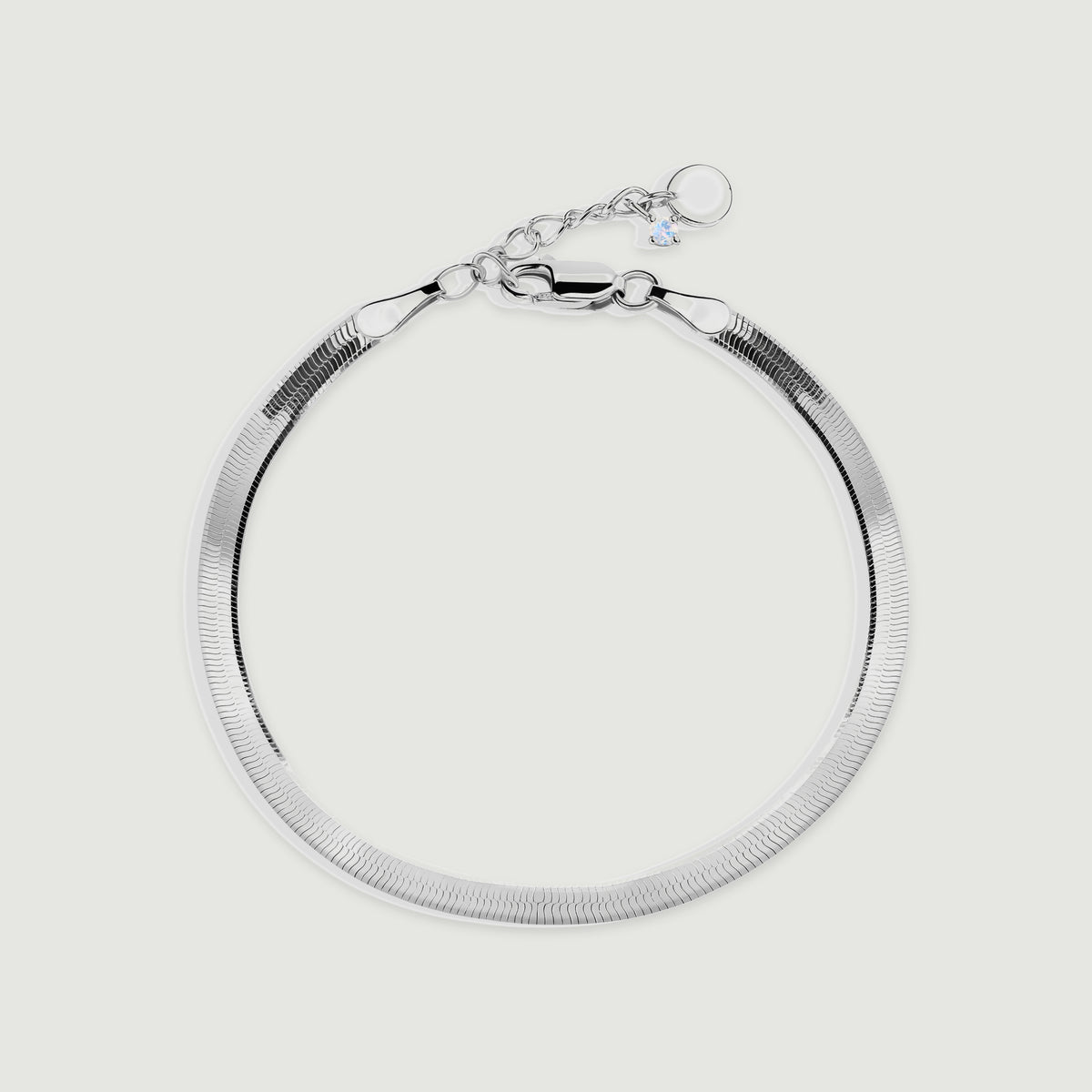 A silver herringbone bracelet forms a rounded loop with its clasp and extension chain visible on a light gray surface.