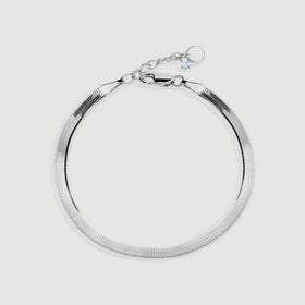 A silver herringbone bracelet forms a rounded loop with its clasp and extension chain visible on a light gray surface.