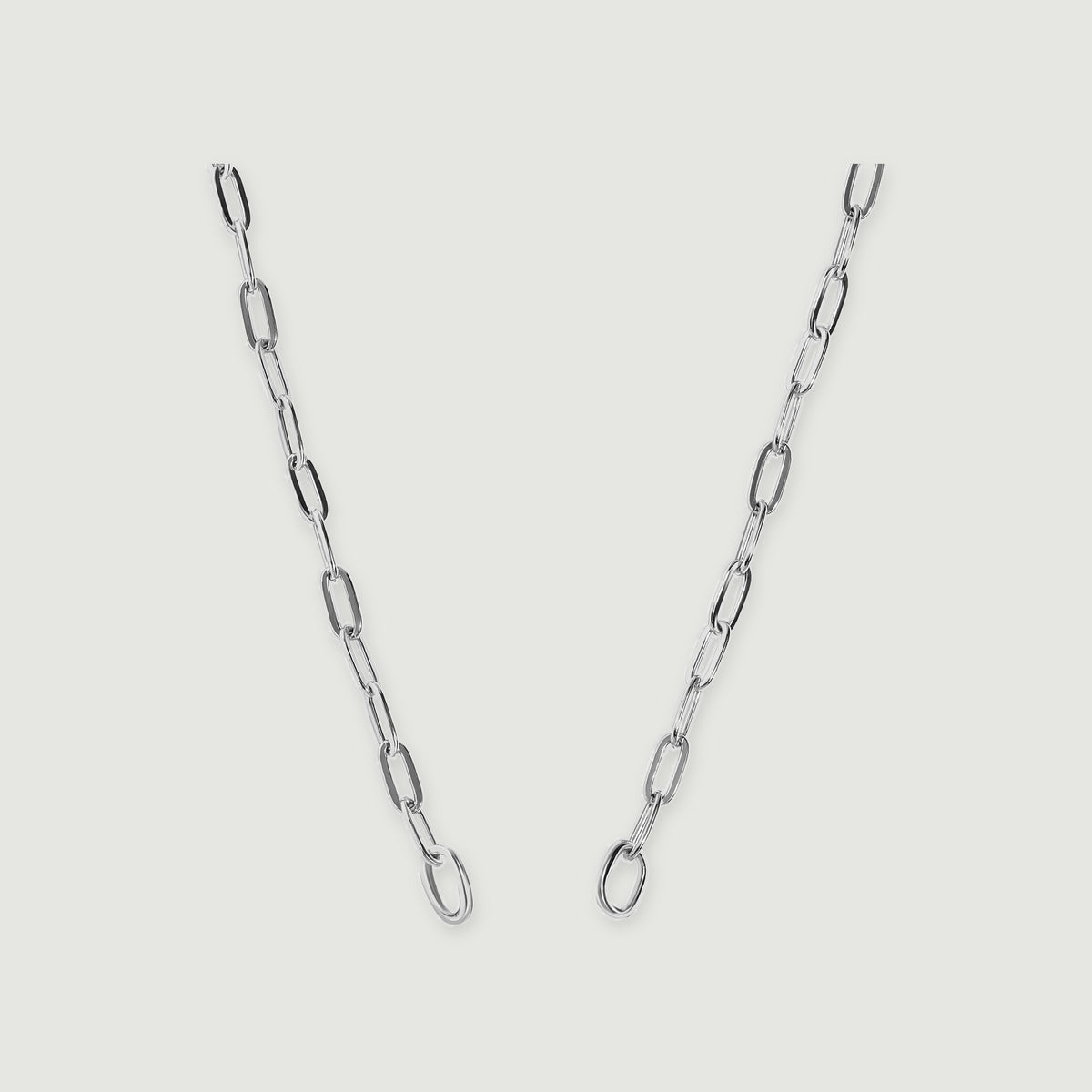 A polished silver chain with elongated links and two round end rings is centered on a pale grey surface.