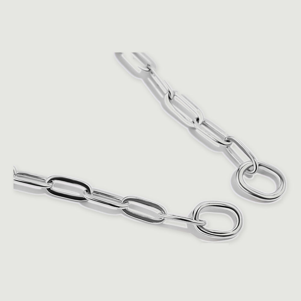 Two silver chain ends with smooth round rings lie diagonally on a light grey surface.