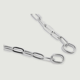 Two silver chain ends with smooth round rings lie diagonally on a light grey surface.
