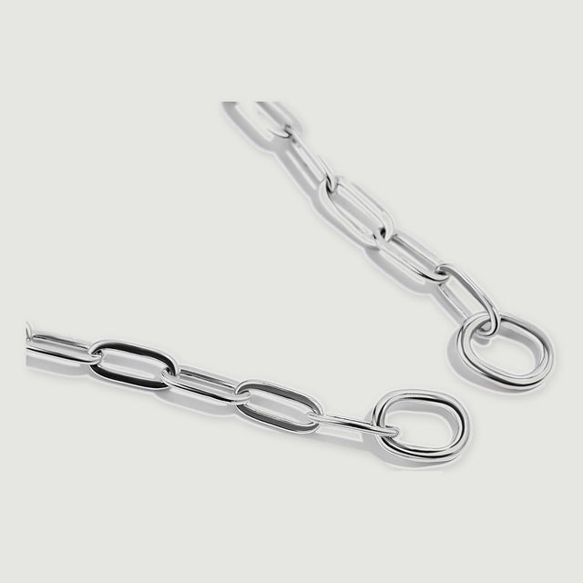Two silver chain ends with smooth round rings lie diagonally on a light grey surface.